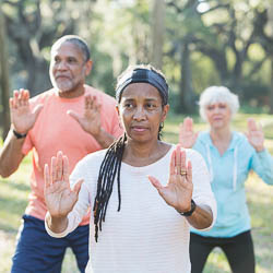 Black woman, black man, and white woman doing tai chi in park